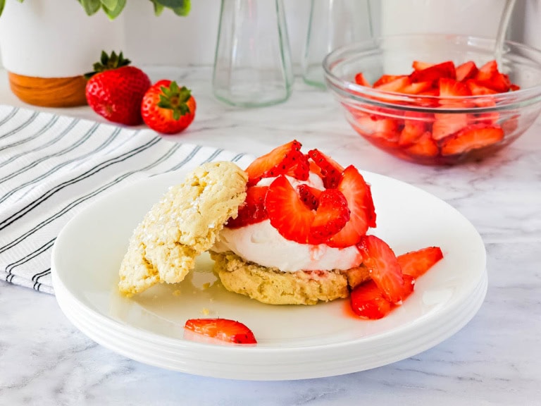 White plate with strawberry shortcake and strawberries in a bowl in the background