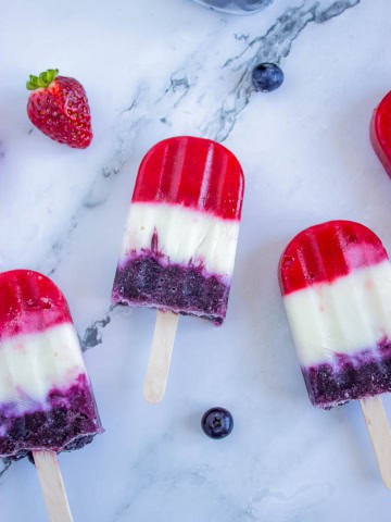 Red white and blue popsicles on white background with blueberries and strawberries around them