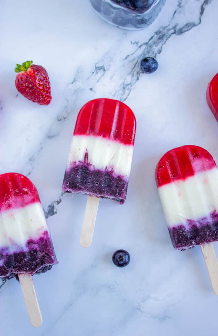 Red white and blue popsicles on white background with blueberries and strawberries around them