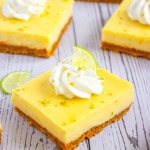 Close up of key lime pie bar on wooden background topped with whipped cream, lime slice and lime zest.