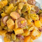 Potatoes, green beans, onions and sausage on white plate.