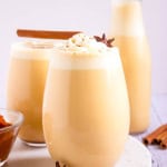 Three glasses of pumpkin spice eggnog with cinnamon sticks and pumpkin spice on the side.