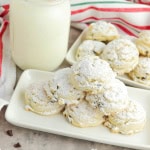 Gluten free snowball cookies on a white plate with glass of milk beside and a red, white and green strip towel