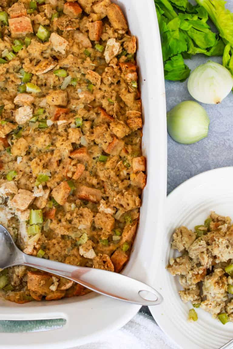 Casserole dish with gluten free thanksgiving stuffing and a metal spoon with plate next to dish with stuffing on it