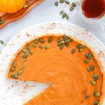 Pumpkin pie on a white plate with pumpkin seeds scattered around it.