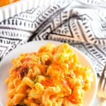 A plate of gluten free macaroni and cheese on white with black and white towel in background.