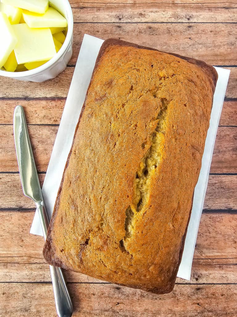 Loaf of gluten free banana bread on wooden background with knife and butter aside.