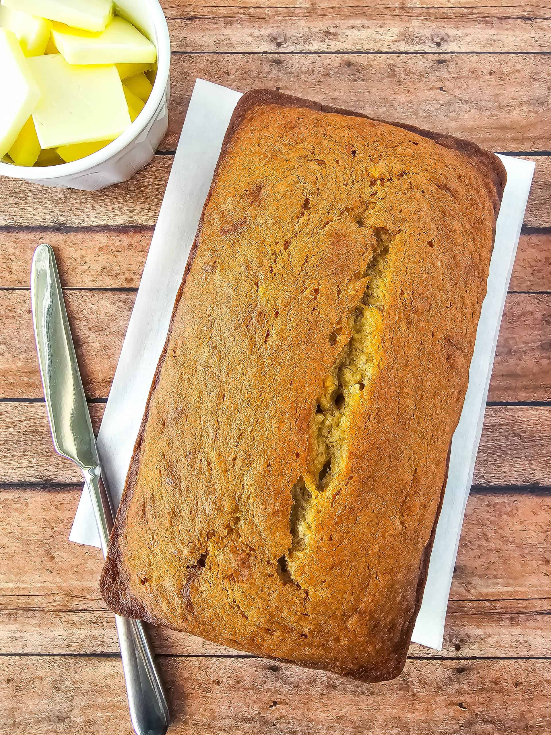 Loaf of gluten free banana bread on wooden background with knife and butter aside.