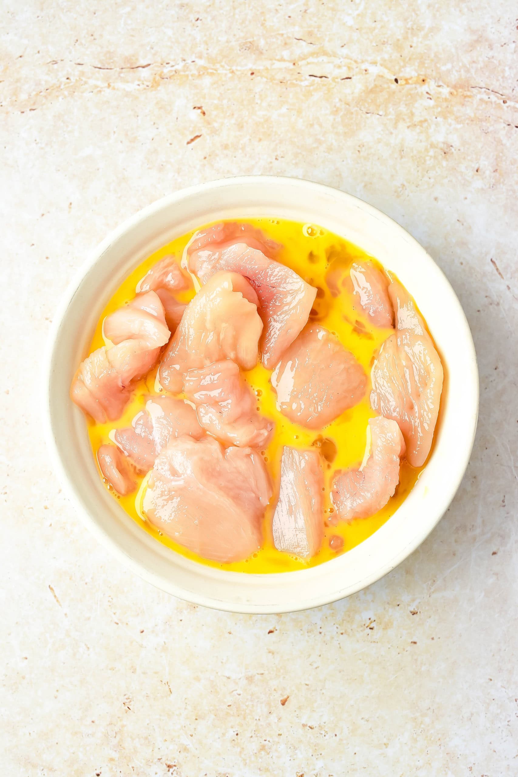 A white bowl with chicken pieces and egg wash mixture