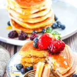 Two plates with stacks of pancakes that are topped with fresh fruit and maple syrup