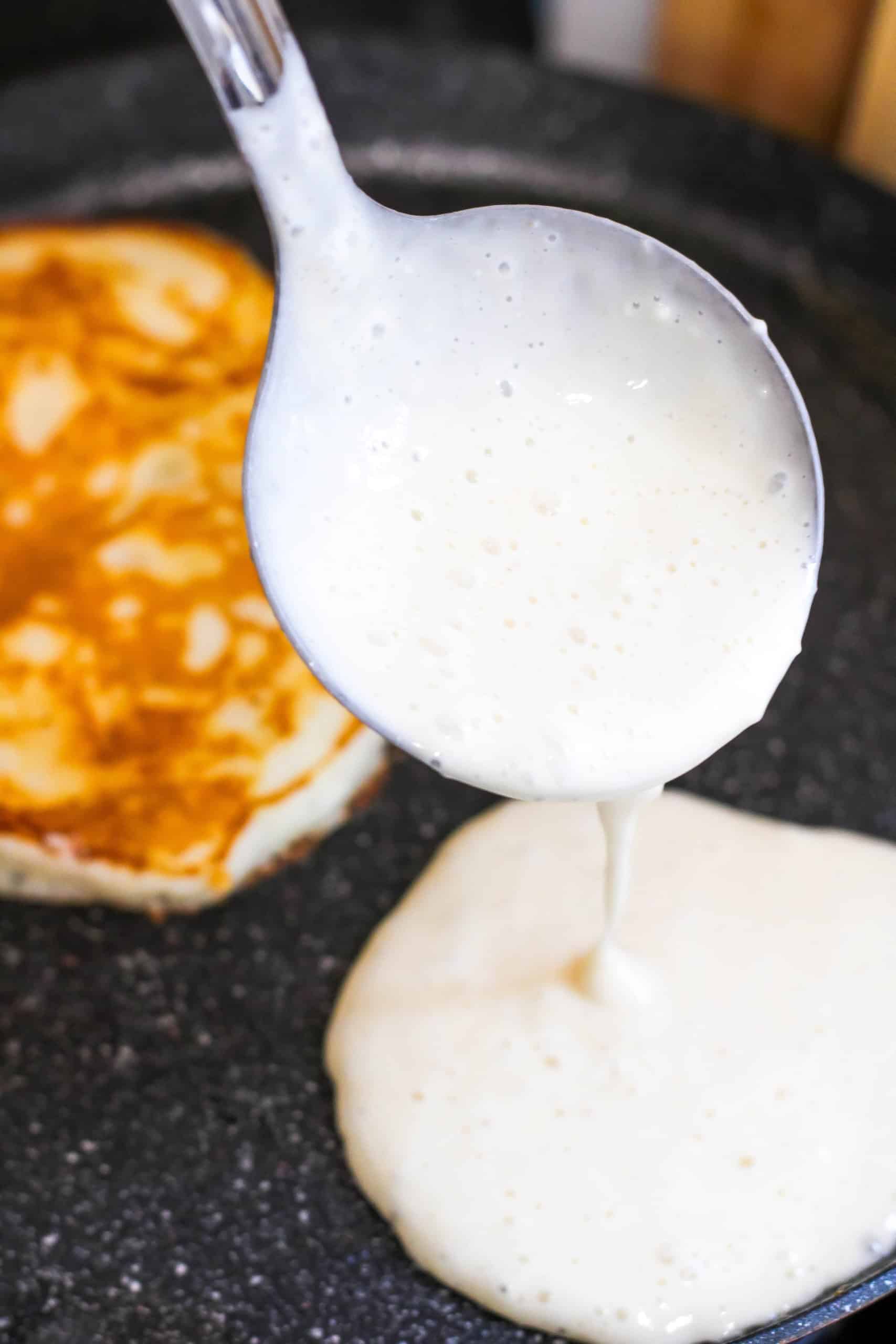 Batter being poured on pan with one pancake finishing cooking on the pan.