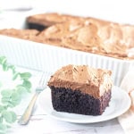 A piece of gluten free chocolate cake on white plate in front of baking pan with chocolate cake.
