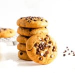 A stack of soft baked gluten free chocolate chip cookies with a few chocolate chips on the side.