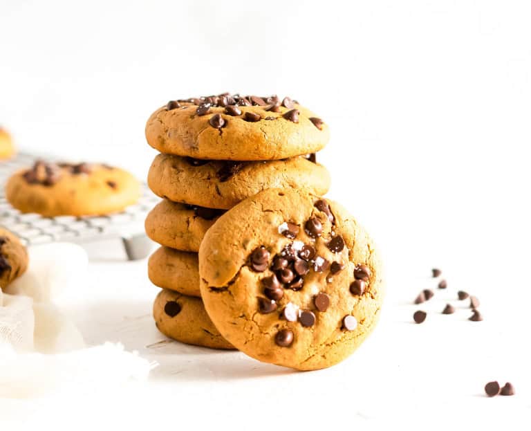 A stack of soft baked gluten free chocolate chip cookies with a few chocolate chips on the side.