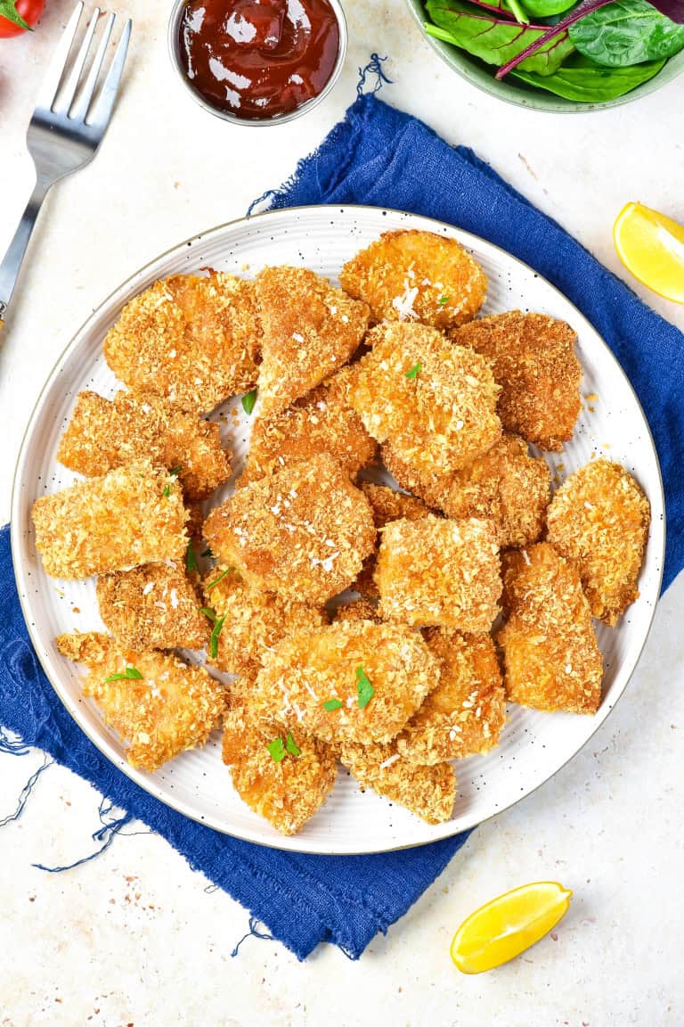 White plate on a blue napkin full of chicken nuggets