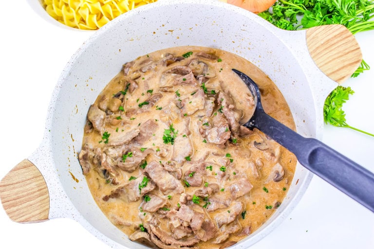 Gluten free beef stroganoff in the white dutch oven with black spoon