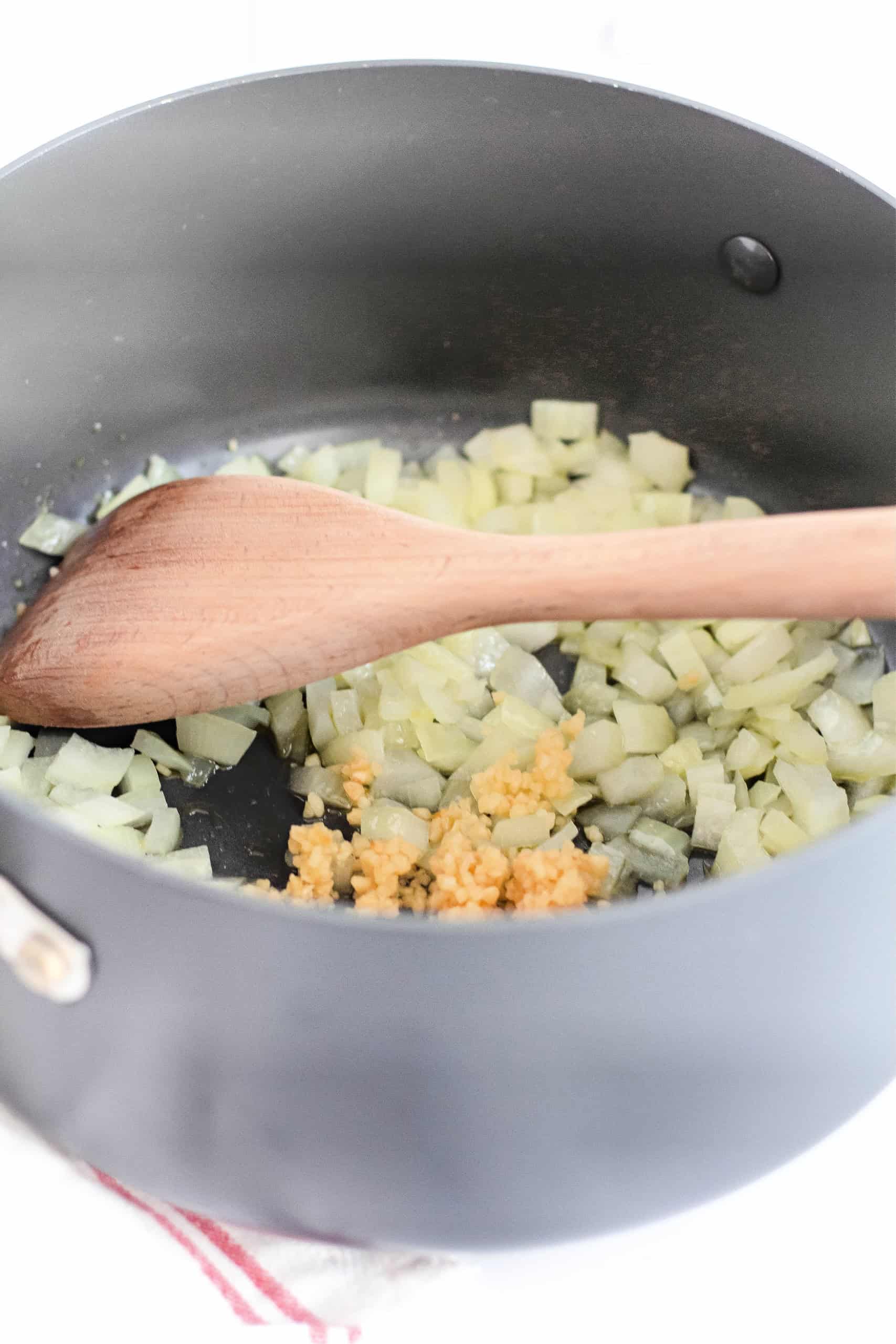 A pot with diced onions cooking and wooden spoon