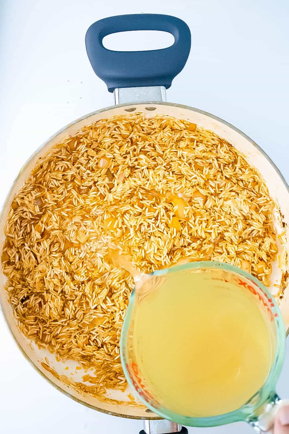 Rice added in with the onions and butter then broth being poured into skillet