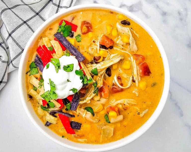 Bowl of chicken enchilada soup in white bowl with black and white towel in corner.