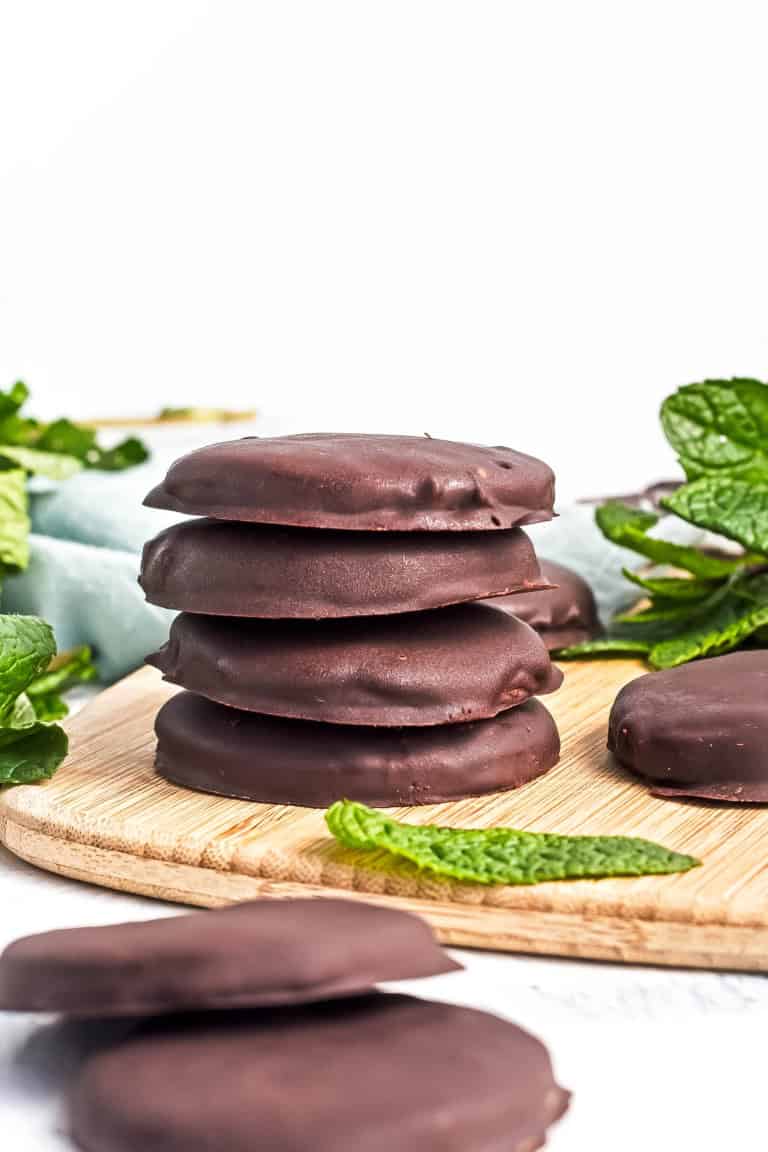 A stack of gluten free thin mint cookies on a wooden board with mint leaves around.