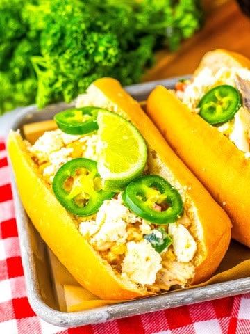 A gluten free hot dog bun with mexican street corn chicken salad on a tray with cilantro behind