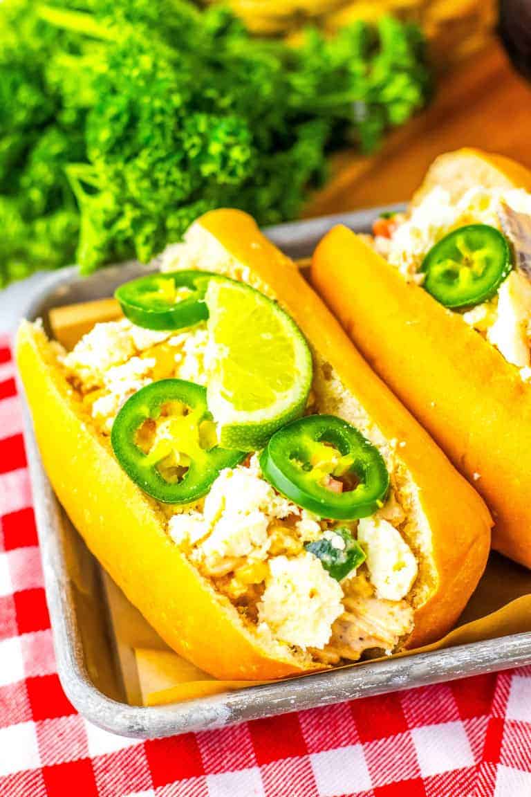 A gluten free hot dog bun with mexican street corn chicken salad on a tray with cilantro behind