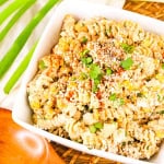 White bowl with mexican street corn pasta salad with wooden spoon and green onion stalk