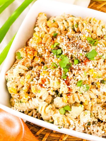 White bowl with mexican street corn pasta salad with wooden spoon and green onion stalk