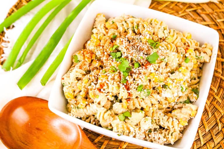 White bowl with mexican street corn pasta salad with wooden spoon and green onion stalk