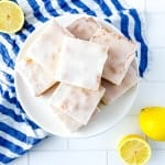 A white plate with lemon brownies along with a white/blue strip towel and lemon