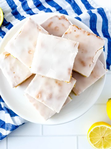 A white plate with lemon brownies along with a white/blue strip towel and lemon