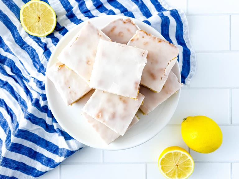 A white plate with lemon brownies along with a white/blue strip towel and lemon