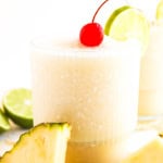 A glass of a pina colada mocktail with a cherry on tip and lime slice.