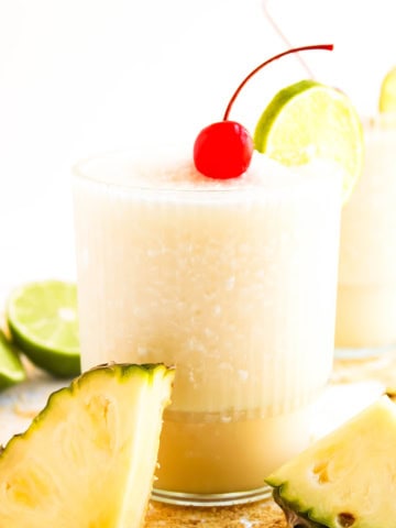 A glass of a pina colada mocktail with a cherry on tip and lime slice.