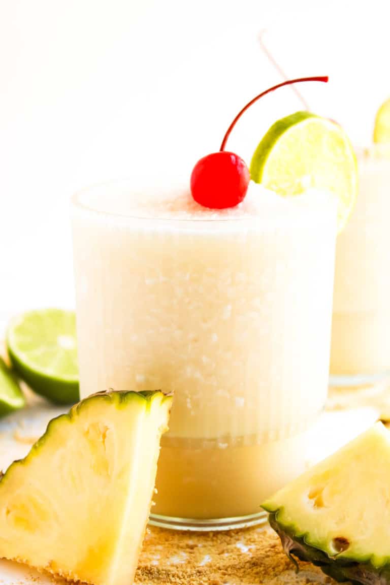 A glass of a pina colada mocktail with a cherry on tip and lime slice.