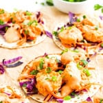 Three bang bang shrimp tacos on tan cloth.