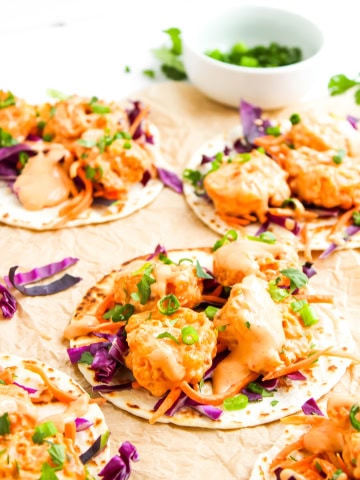 Three bang bang shrimp tacos on tan cloth.