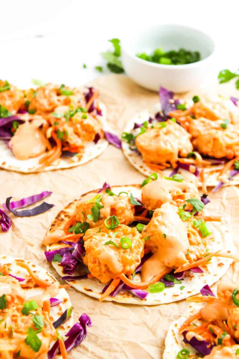 Three bang bang shrimp tacos on tan cloth.