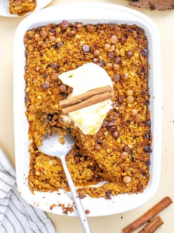 Baking dish with gluten free pumpkin crisp topped with whipped cream and cinnamon sticks.