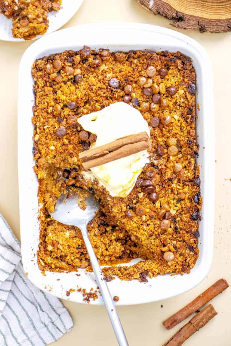 Baking dish with gluten free pumpkin crisp topped with whipped cream and cinnamon sticks.